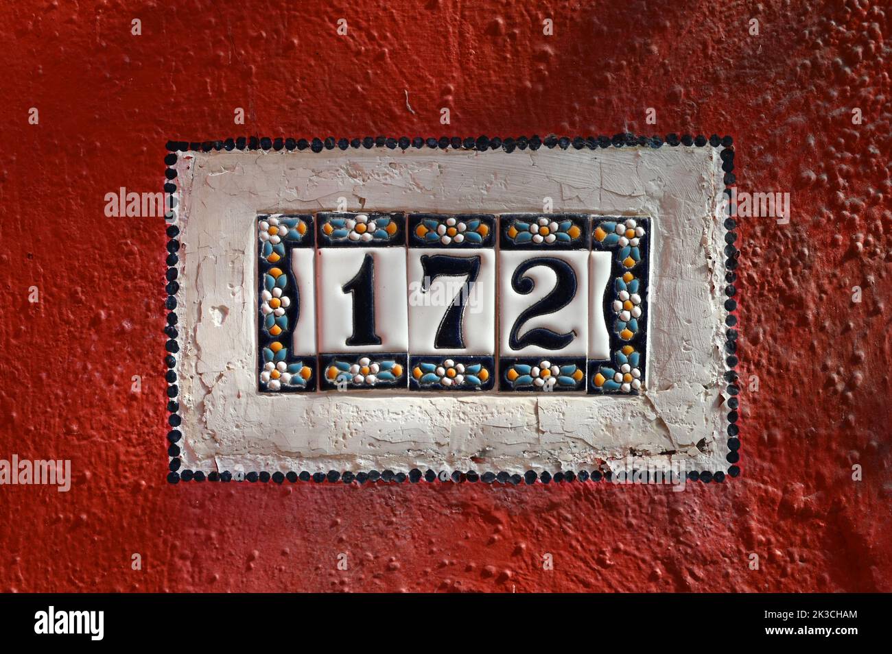 Vintage 172 number plate made of ceramic pieces and attached to crumbling red wall of house Stock Photo