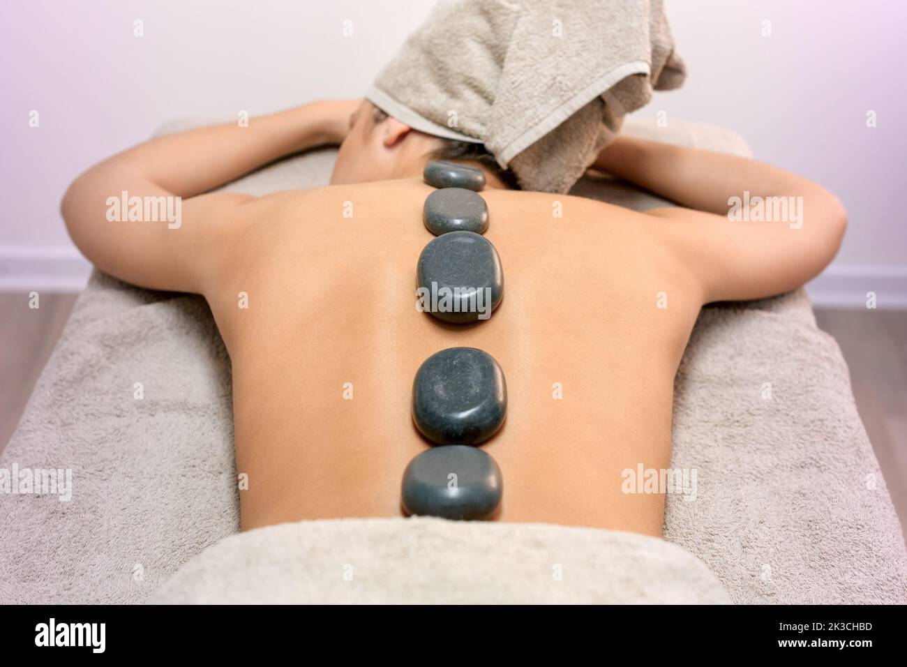 High angle of unrecognizable topless female with hot stones on back lying on table during massage session in spa salon Stock Photo