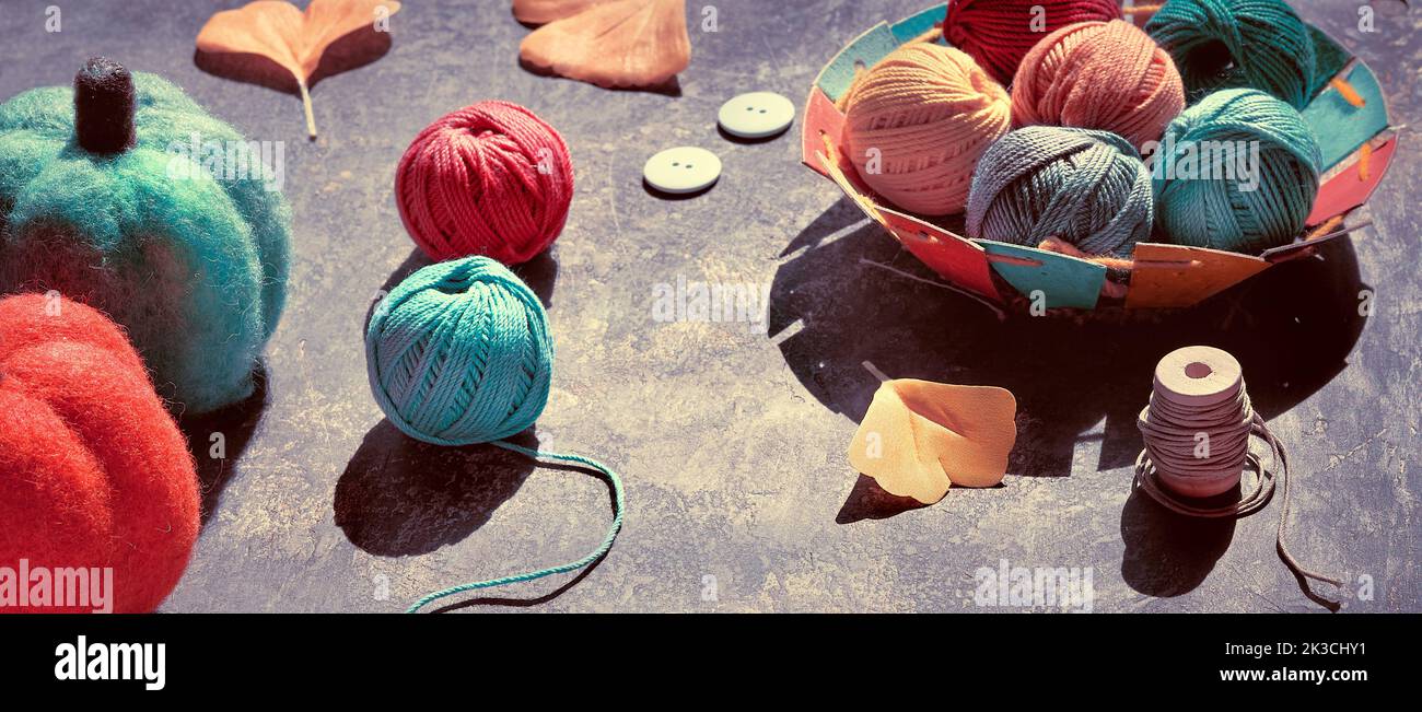 Panoramic banner with craft materials for knitting and crochet on dark table. Yarn balls, decorative felt pumpkins, Fall leaves with shadows. Stock Photo