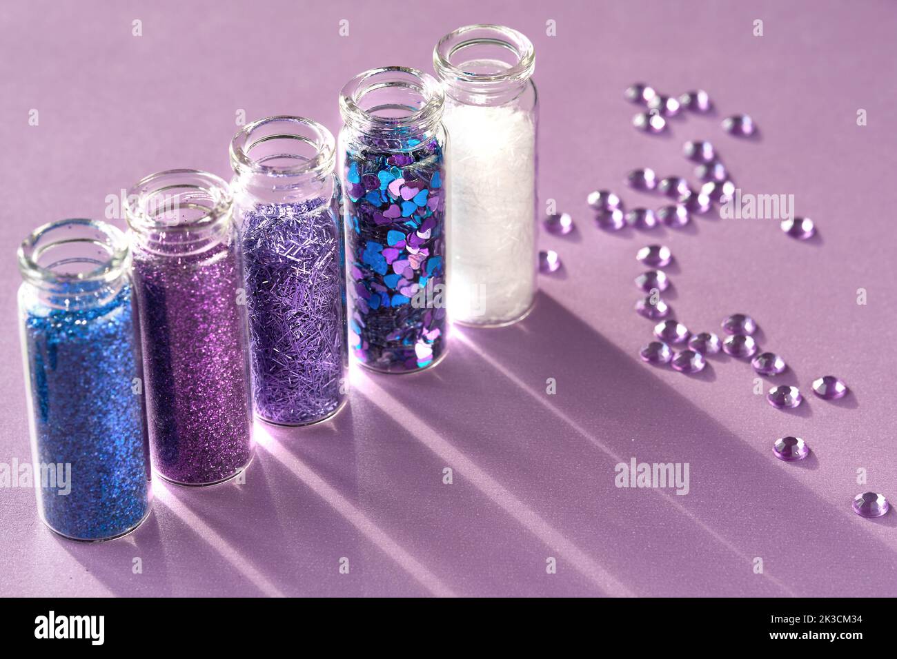 All kinds of glitter products on pink sparkling background. Close-up on vials, bottles with various glitter makeup in neon pink, blue and turquoise Stock Photo