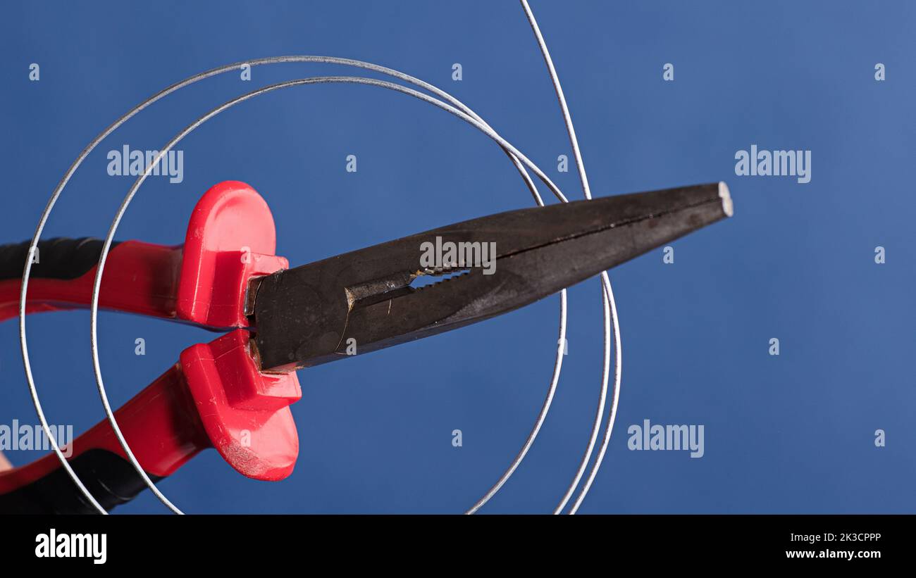 Cutting and holding pliers with coil of wire, blue background Stock Photo