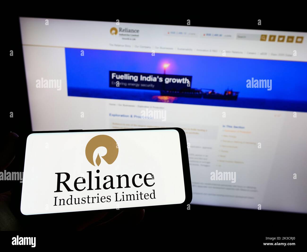 Person holding smartphone with logo of Indian company Reliance Industries Limited on screen in front of website. Focus on phone display. Stock Photo