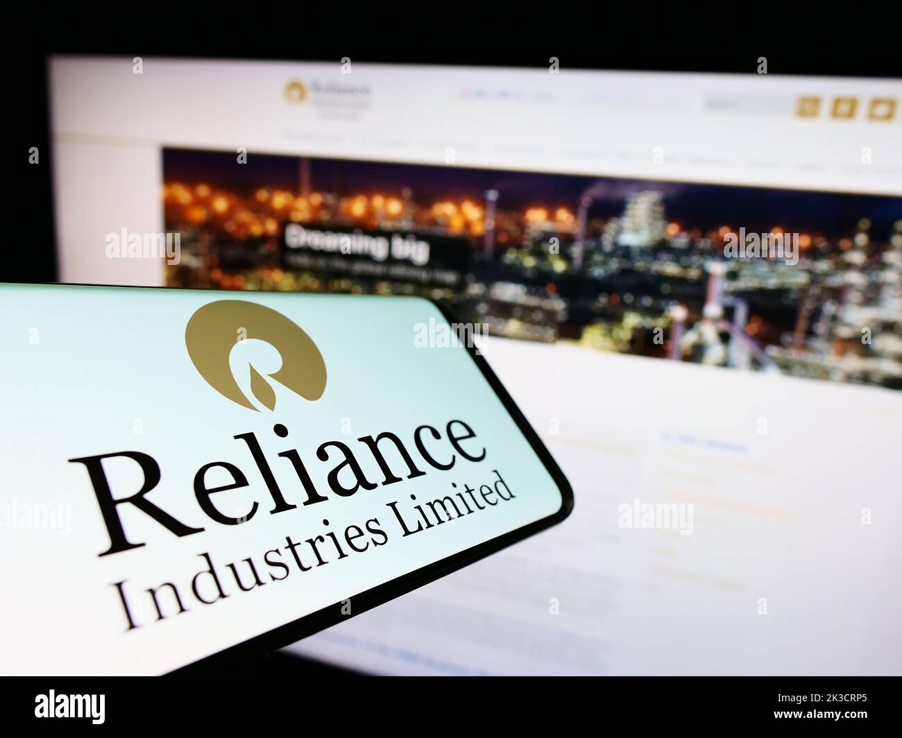 Mobile phone with logo of Indian company Reliance Industries Limited on screen in front of website. Focus on center-right of phone display. Stock Photo