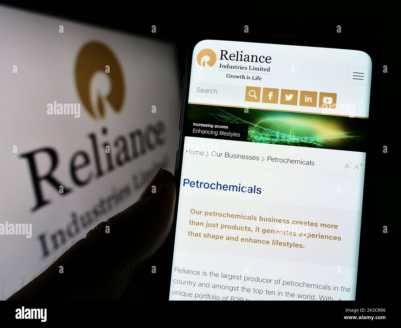 Person holding cellphone with webpage of Indian company Reliance Industries Limited on screen in front of logo. Focus on center of phone display. Stock Photo