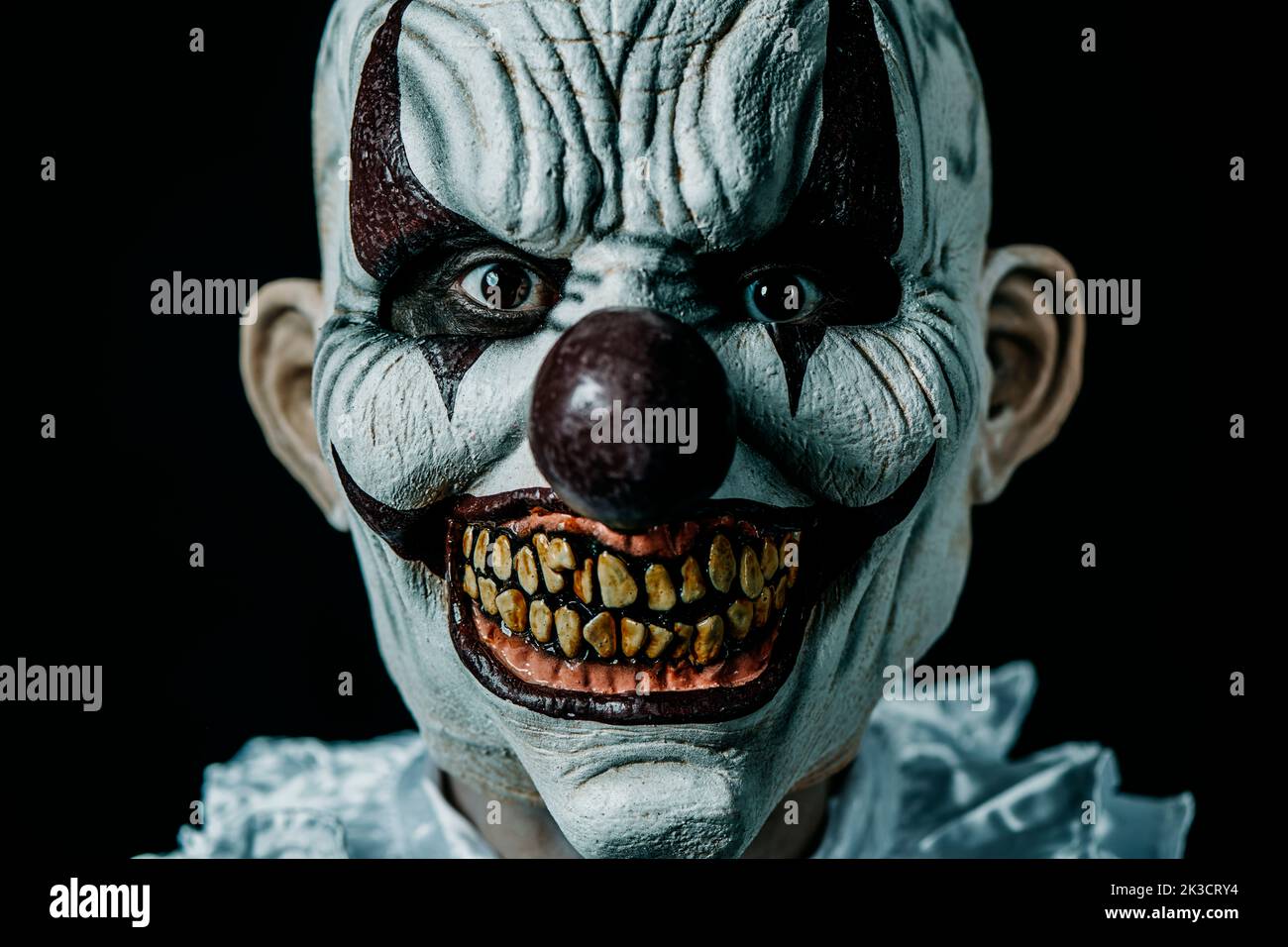 closeup of a creepy bald evil clown staring at the observer, against a black background Stock Photo