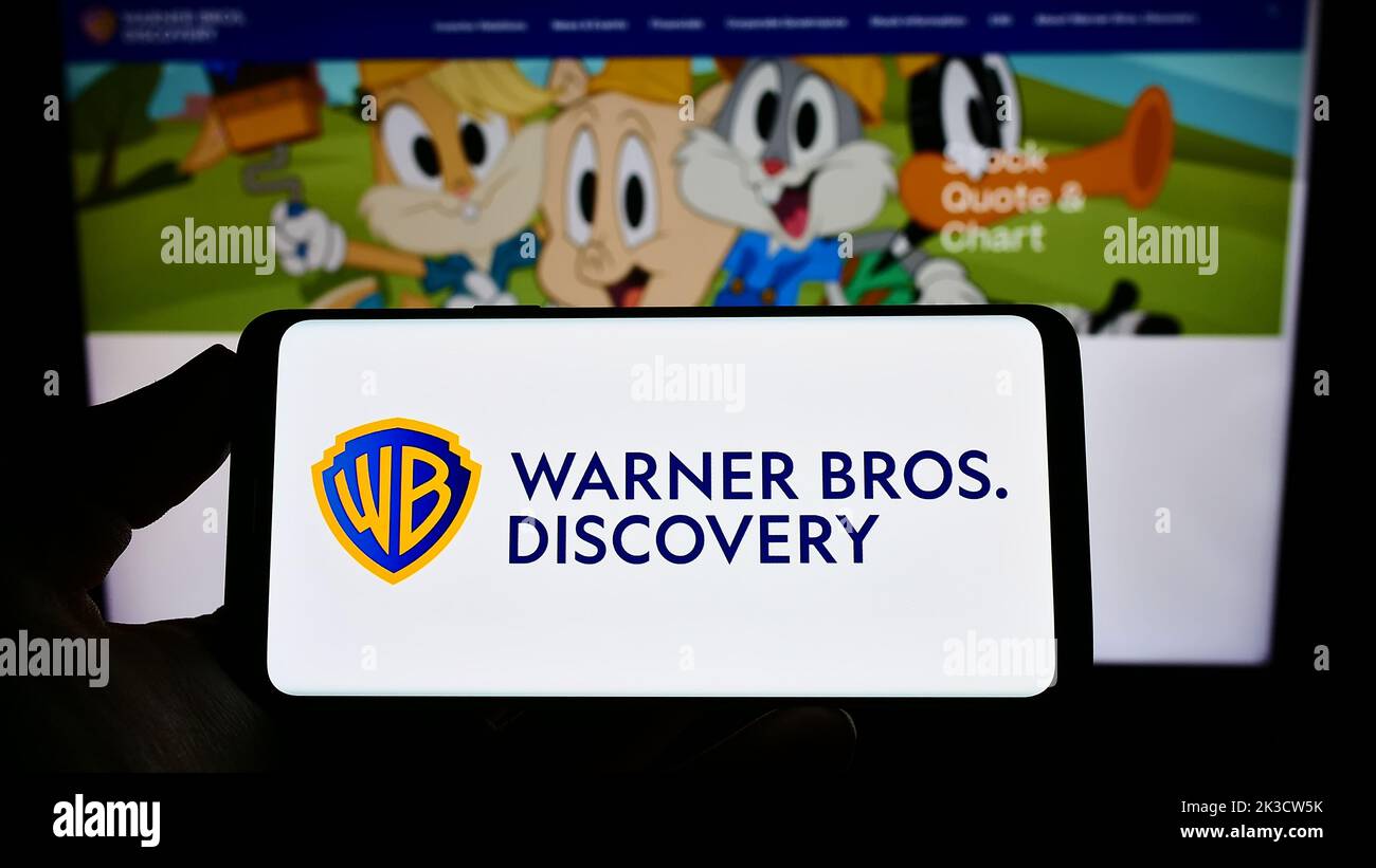 Person holding smartphone with logo of media company Warner Bros. Discovery Inc. (WBD) on screen in front of website. Focus on phone display. Stock Photo