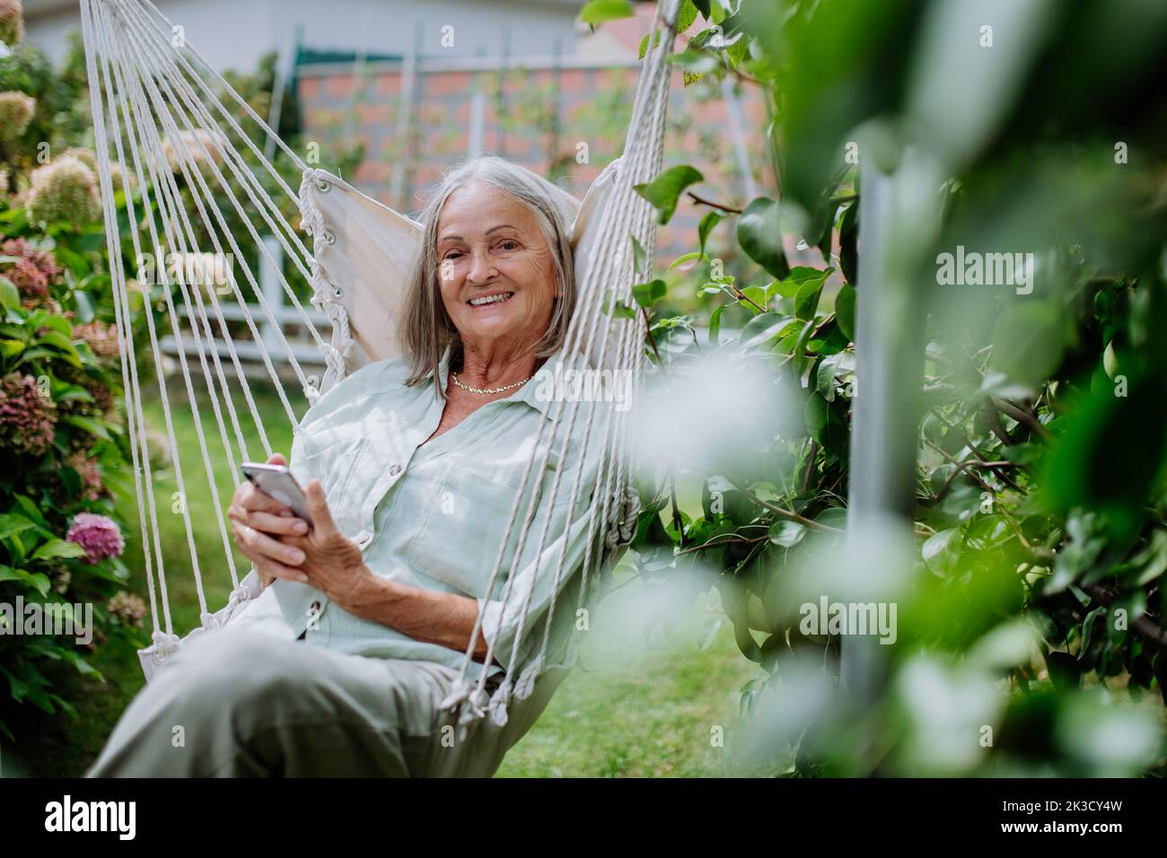 Senior woman relaxing in garden swing with smartphone. Stock Photo