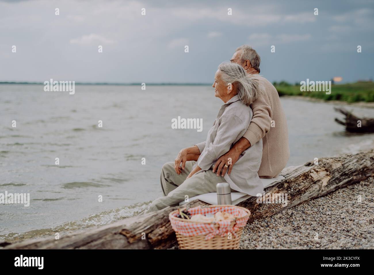 Senior couple sitting with picnic basket and having romantic moment near the autumn sea. Stock Photo