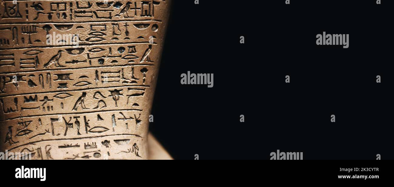 A stone tablet engraved with ancient Egyptian hieroglyphic symbols against a dark black background with copy space Stock Photo