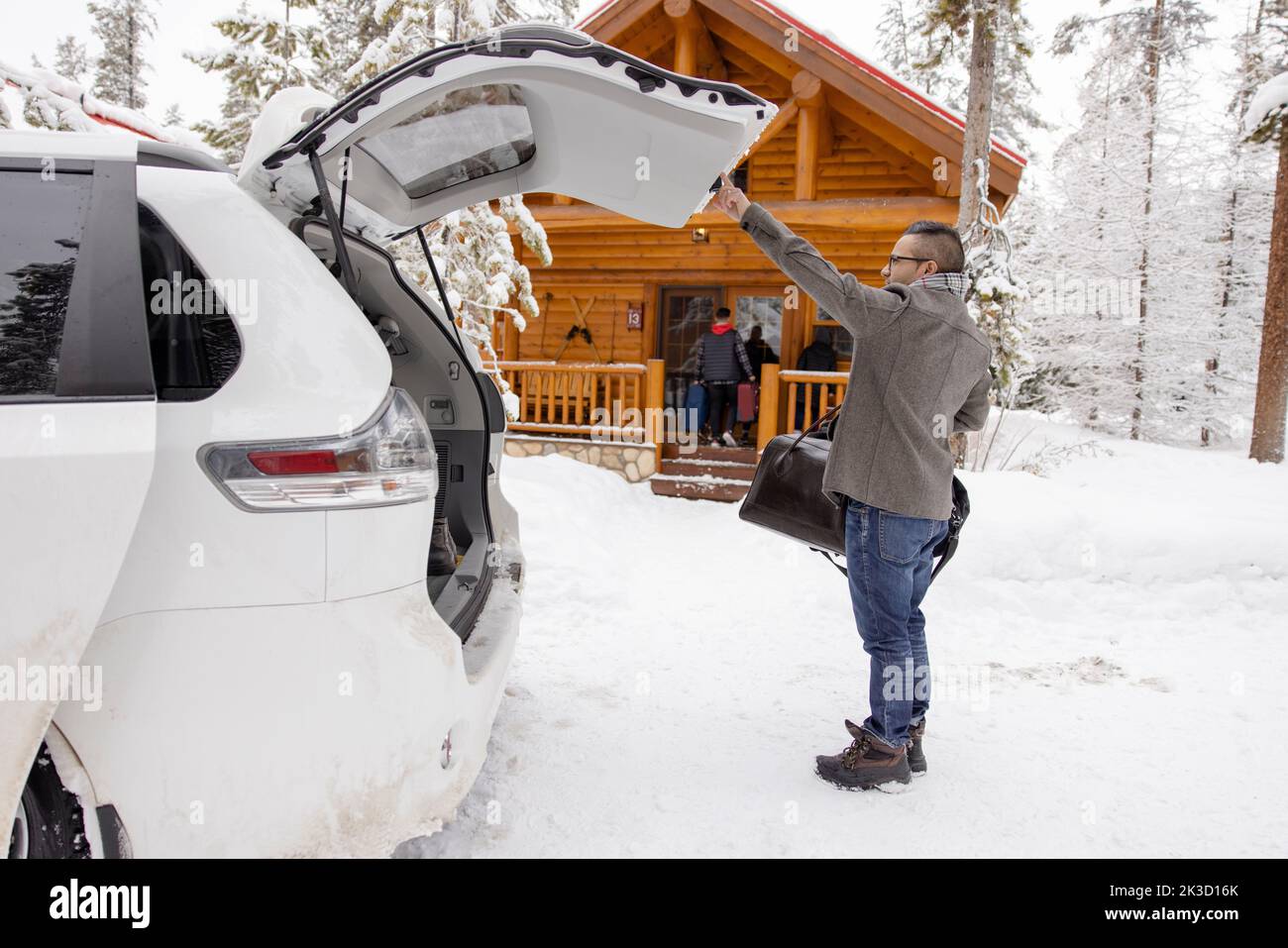 Man arriving and unloading luggage from car outside snowy winter cabin