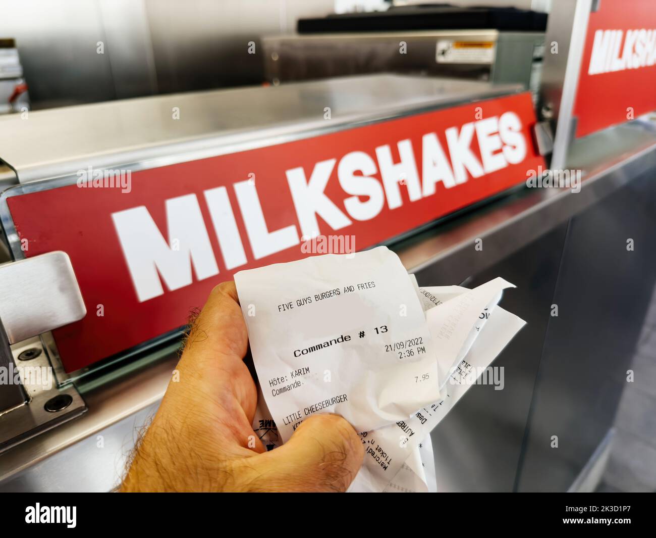 Paris, France - Sep 21, 2022: Five Guys American fast food restaurant with customer holding receipt in front of milkshakes logo - chain with focused on hamburgers, hot dogs, and French fries, and headquartered in Lorton, Virginia, part of Fairfax County. Stock Photo