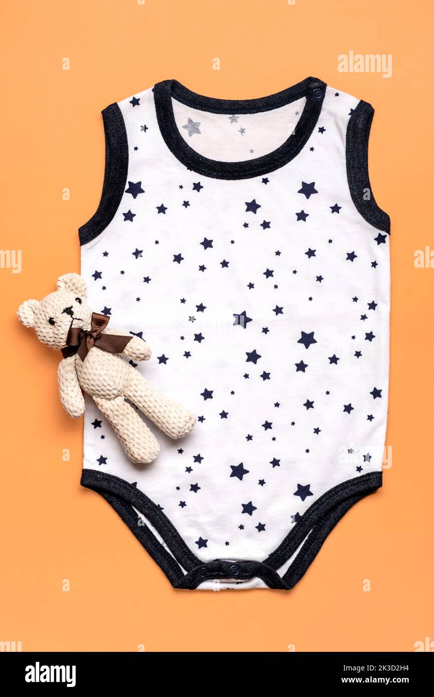 beautiful white clothes with stars for newborn, bear toy isolated on beige background Copy space Concept of childhood, motherhood, fashion textile and newborn Top view Flat lay. Stock Photo