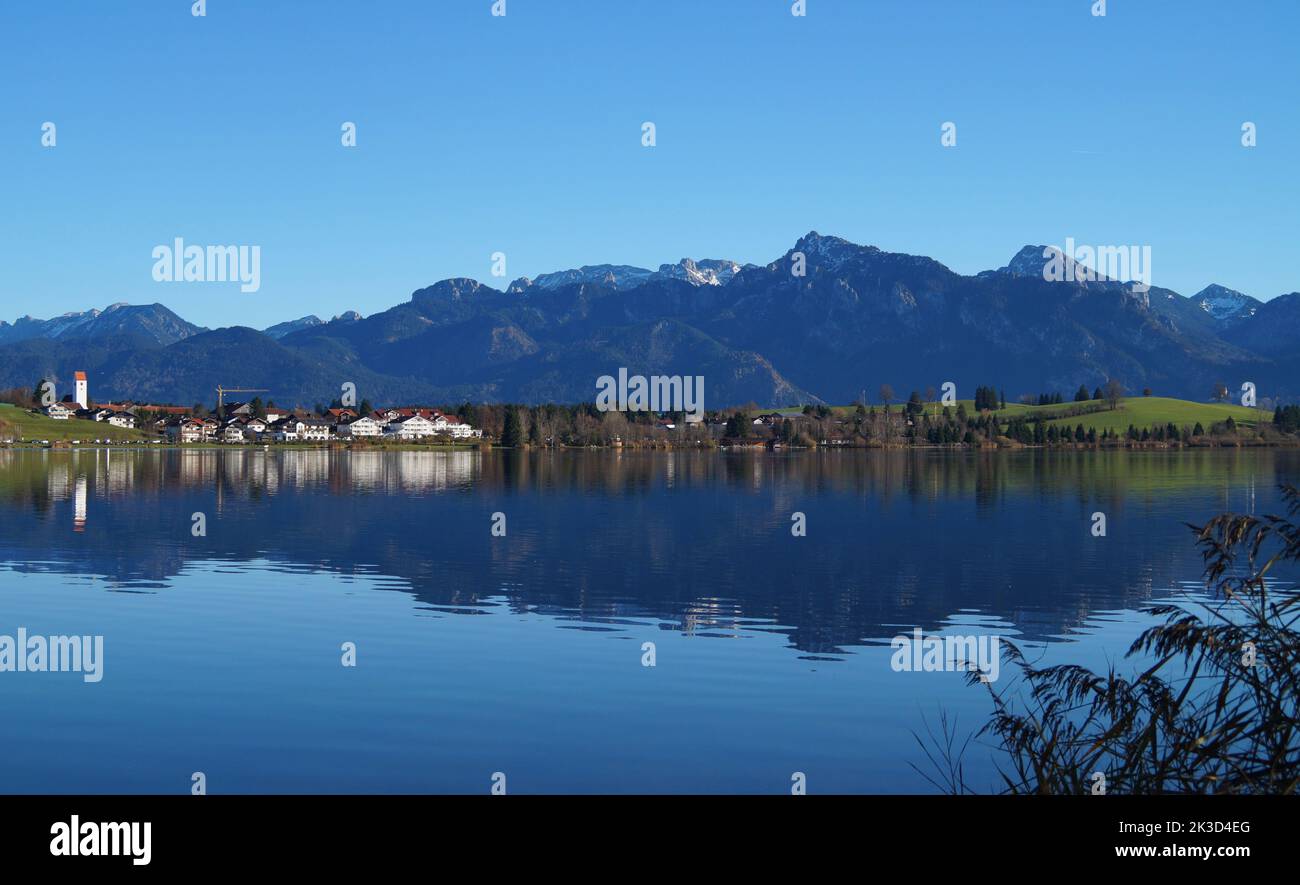 alpine landscape with scenic and calm lake Hopfensee and the Bavarian Alps reflected in the blue lake on a sunny November day (Bavaria, Germany) Stock Photo