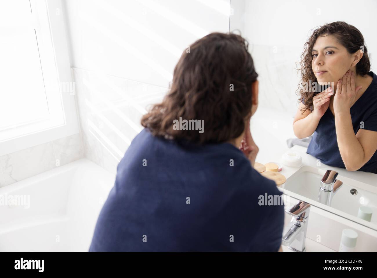 Woman touching neck at bathroom mirror Stock Photo