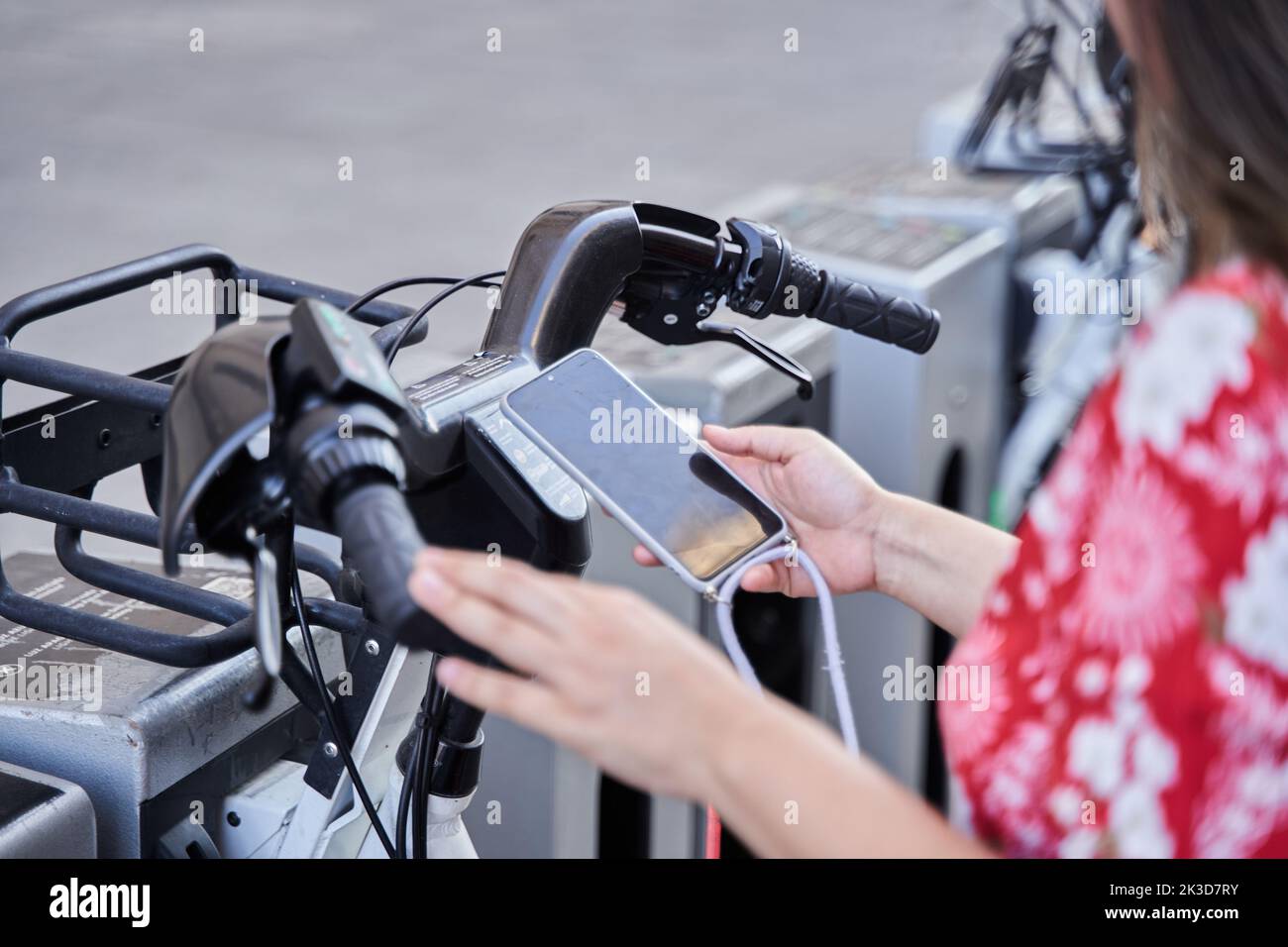 Woman using app on smartphone to unlock electric bike on the street. Driving ecology transportation. Stock Photo