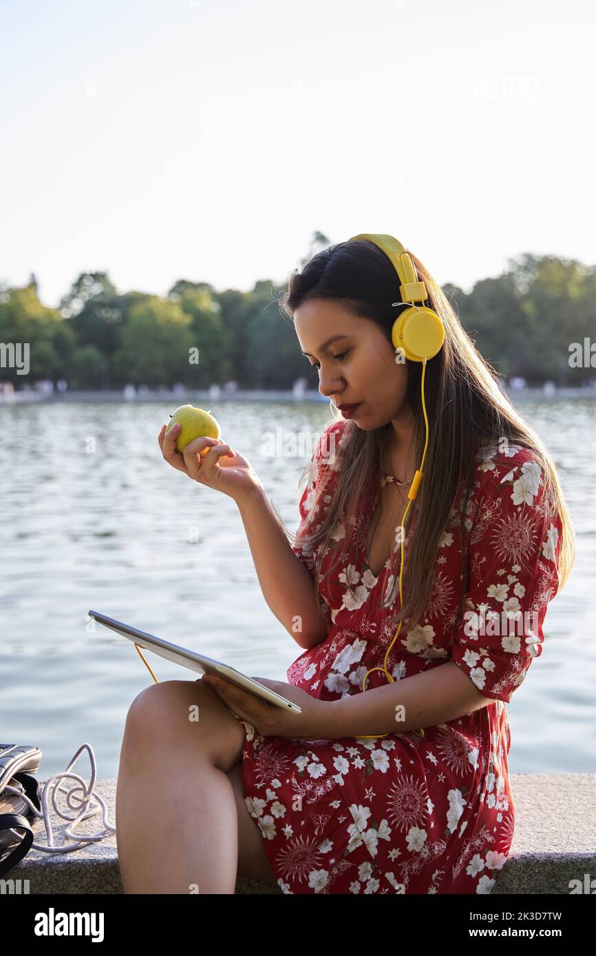 woman looking at a tablet pc with an apple and headphones. young latina spending her free time. Stock Photo