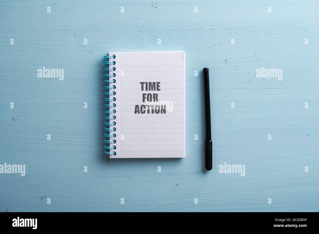 Spiral notebook with a Time for action sign spelled in it and black marker next to it. Over pastel blue wooden background. Stock Photo