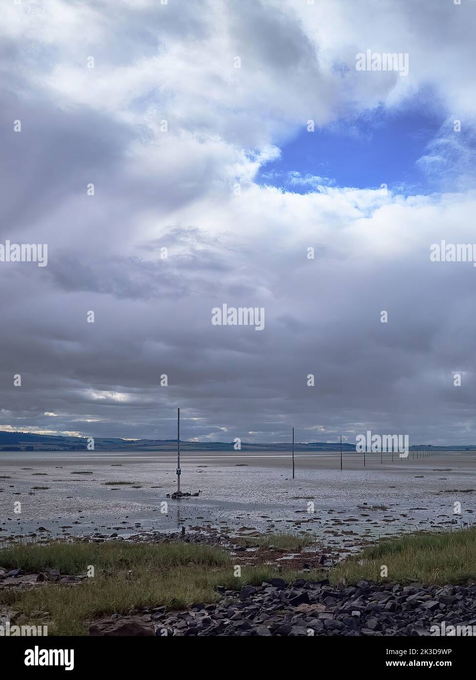 The stark, open space around the Lindisfarne causeway at low tide, marker poles receding into the distance, under a huge clouded sky. Stock Photo