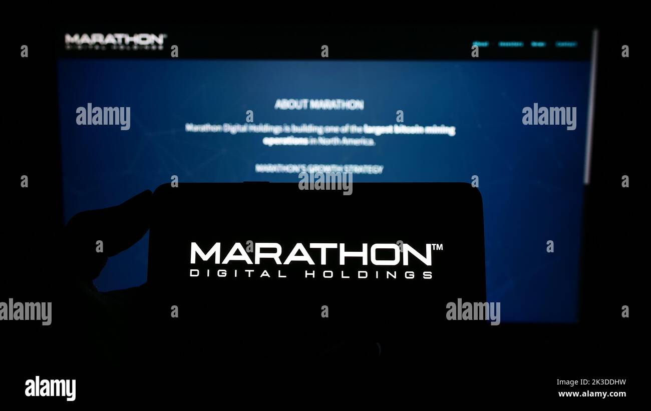 Person holding mobile phone with logo of American company Marathon Digital Holdings Inc. on screen in front of web page. Focus on phone display. Stock Photo