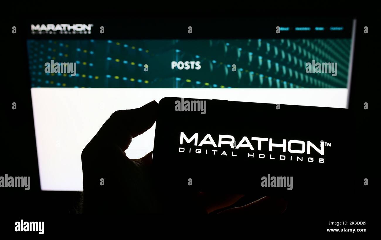 Person holding cellphone with logo of US company Marathon Digital Holdings Inc. on screen in front of business webpage. Focus on phone display. Stock Photo