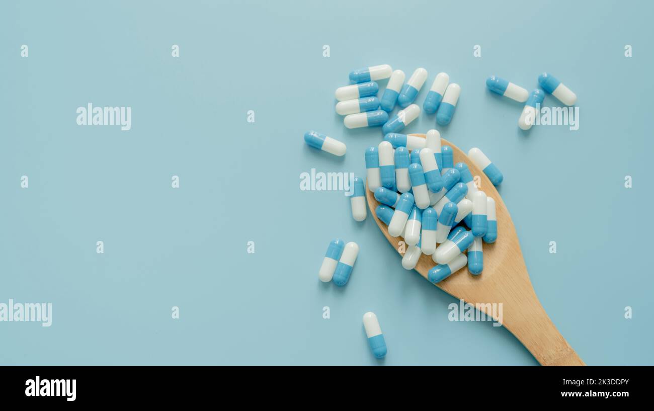 Blue-white antibiotic capsule pills on wooden spoon and blue background. Antibiotic drug resistance. Prescription drug. Medical care. Pharmaceutical Stock Photo