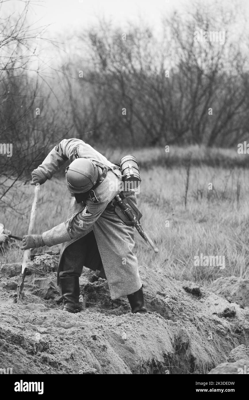 Re-enactor Dressed As German Wehrmacht Infantry Soldier In World War II With Shovel Digs Trench. Defensive Position. German Military Dress Of German Stock Photo
