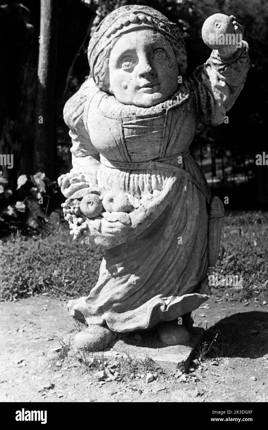 Zwergin mit Obstschürze, symbolisch für den Monat September im Mirabellgarten in  Salzburg, circa 1960. Dwarfess with fruit apron, symbolic for the month of September, around 1960. Stock Photo