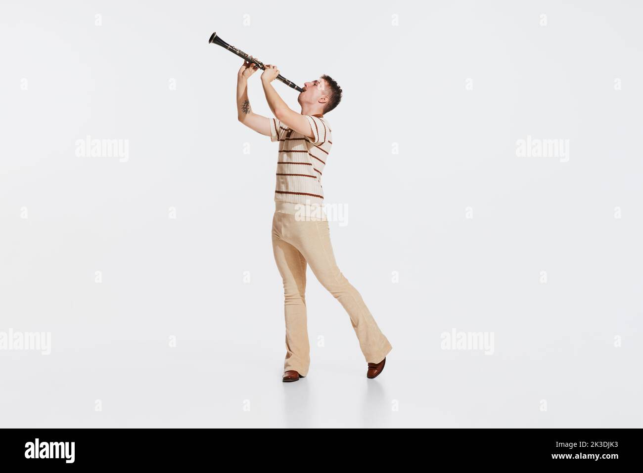 Young man wearing 50s, 60s fashion style clothes playing clarinet on white studio backround. Music, art, inspiration concept Stock Photo