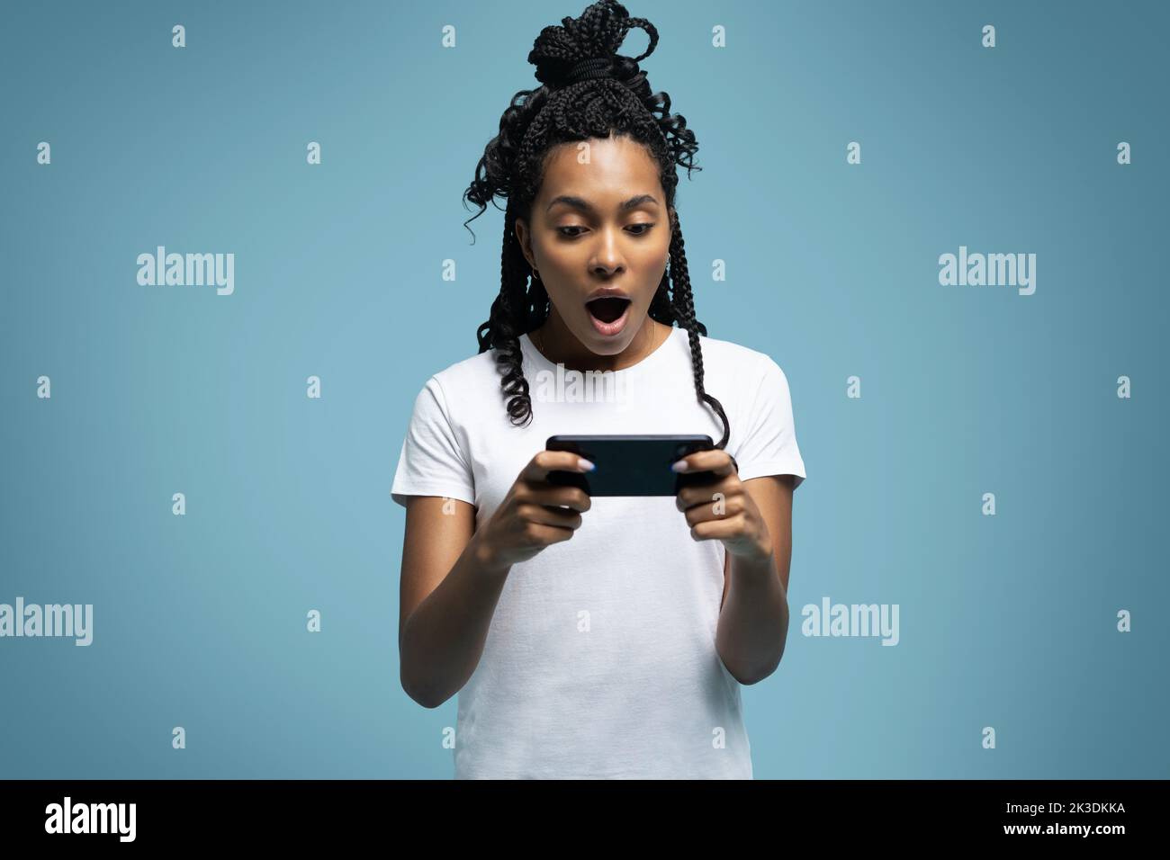 Positive curly haired ethnic woman uses mobile phone checks messages and reads news holds modern cellular in hands looks with curious happy expression Stock Photo