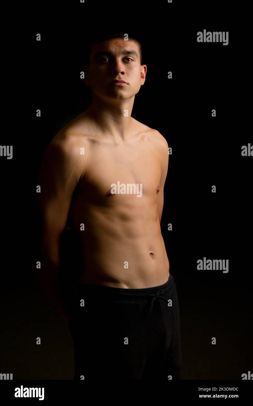 A shirtless 19 year old teenage boy with a black background Stock Photo