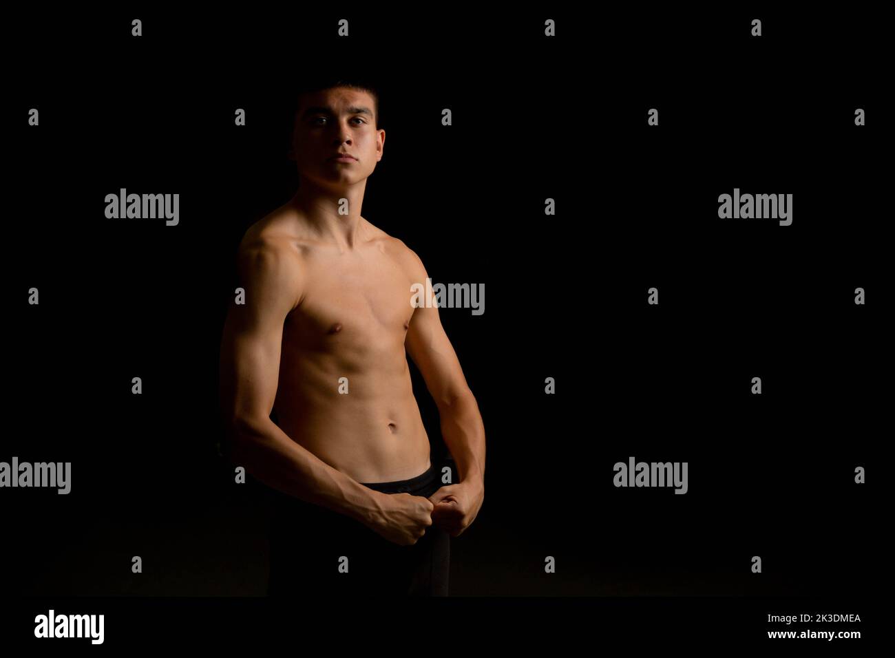 Portrait of a 19 year old shirtless teenage boy on a black background Stock Photo