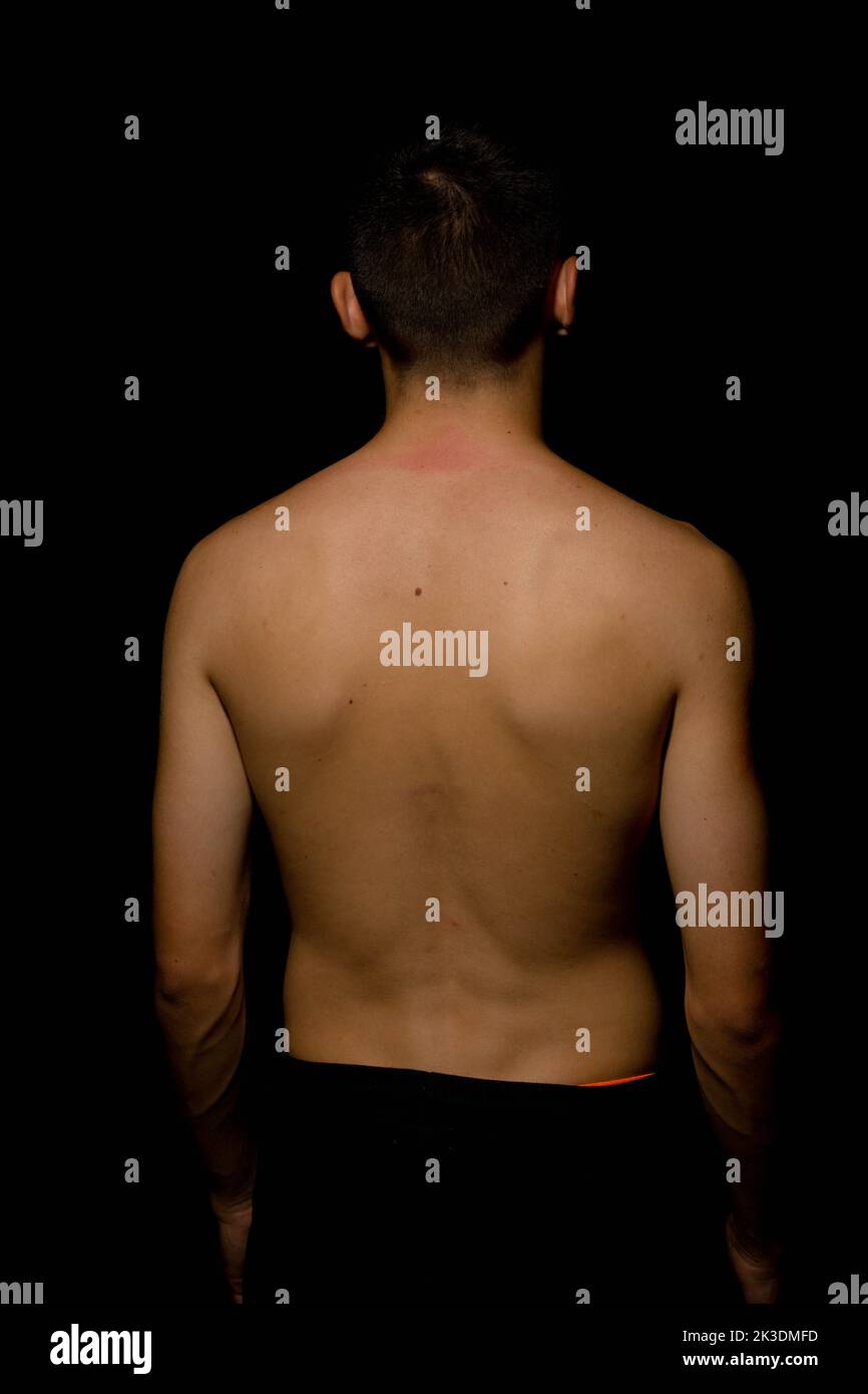 A shirtless 19 year old teenage boy's back against a black background Stock Photo