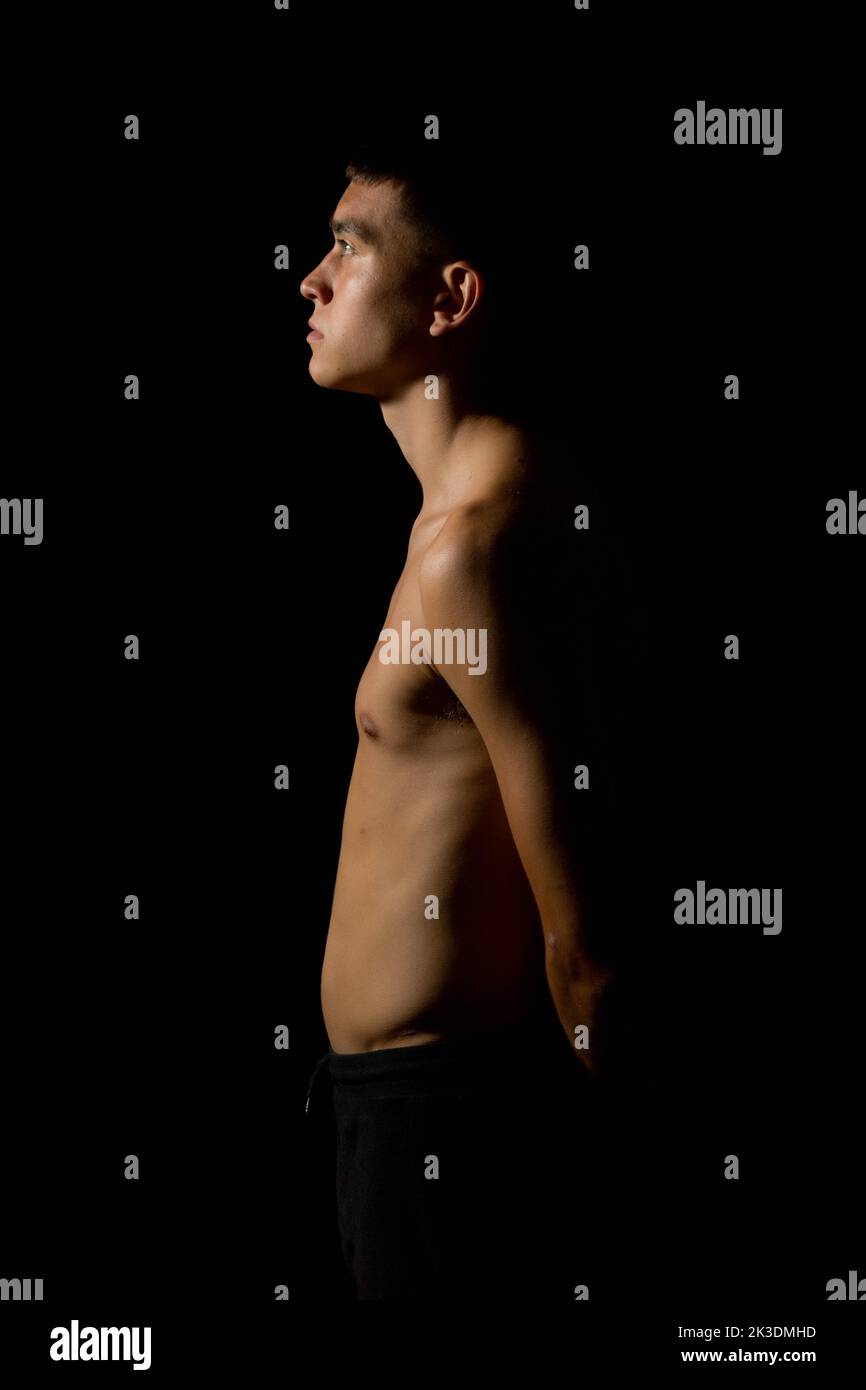 19 year old teen boy's body side view on a black background Stock Photo