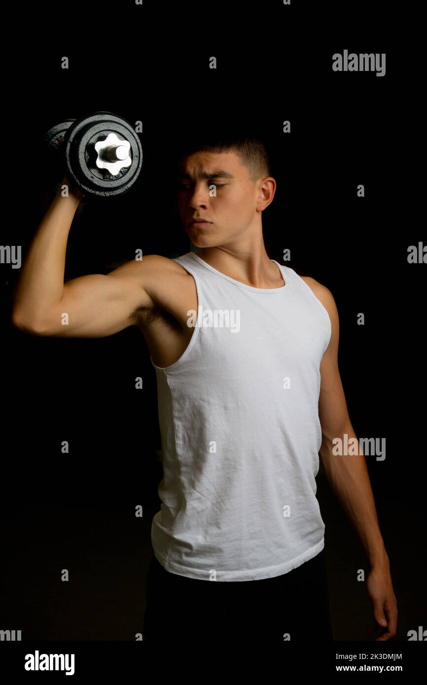 19 year old teenage boy wearing a tank top using a dumbbells Stock Photo