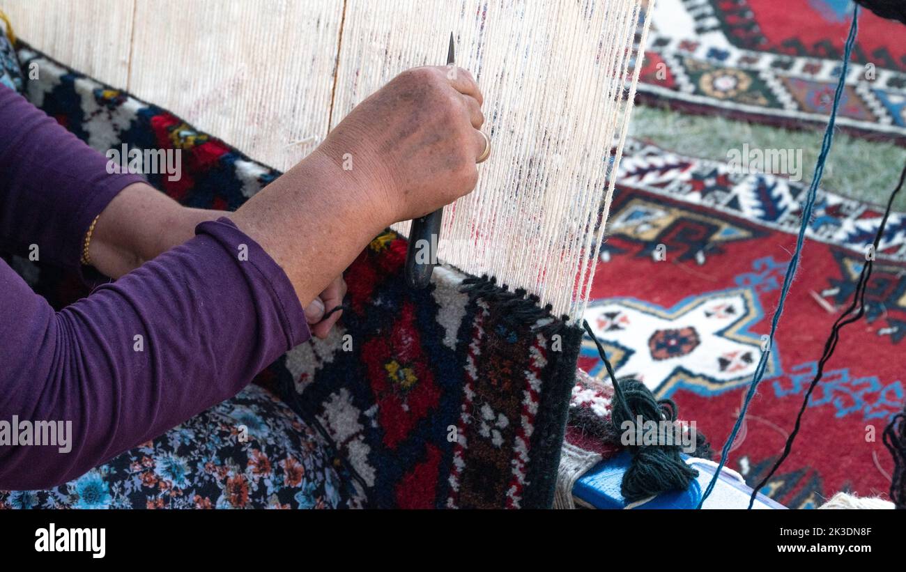 Grandma weaves a carpet on a loom of thread, making a rug Stock Photo