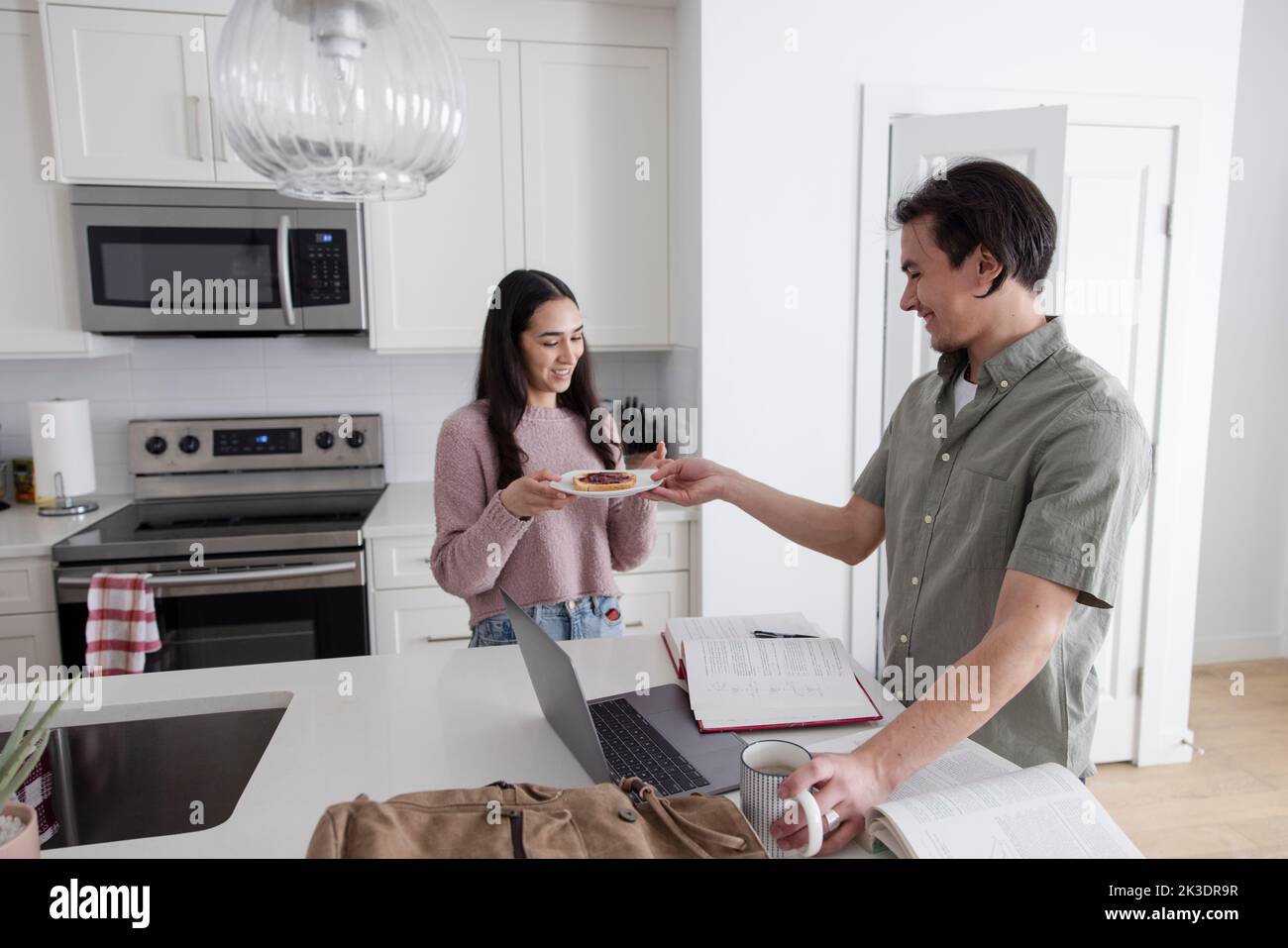 Sister making toast for college student brother studying in kitchen