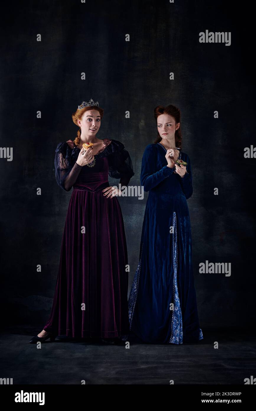 Portrait of two beautiful women in image of queens isolated over dark