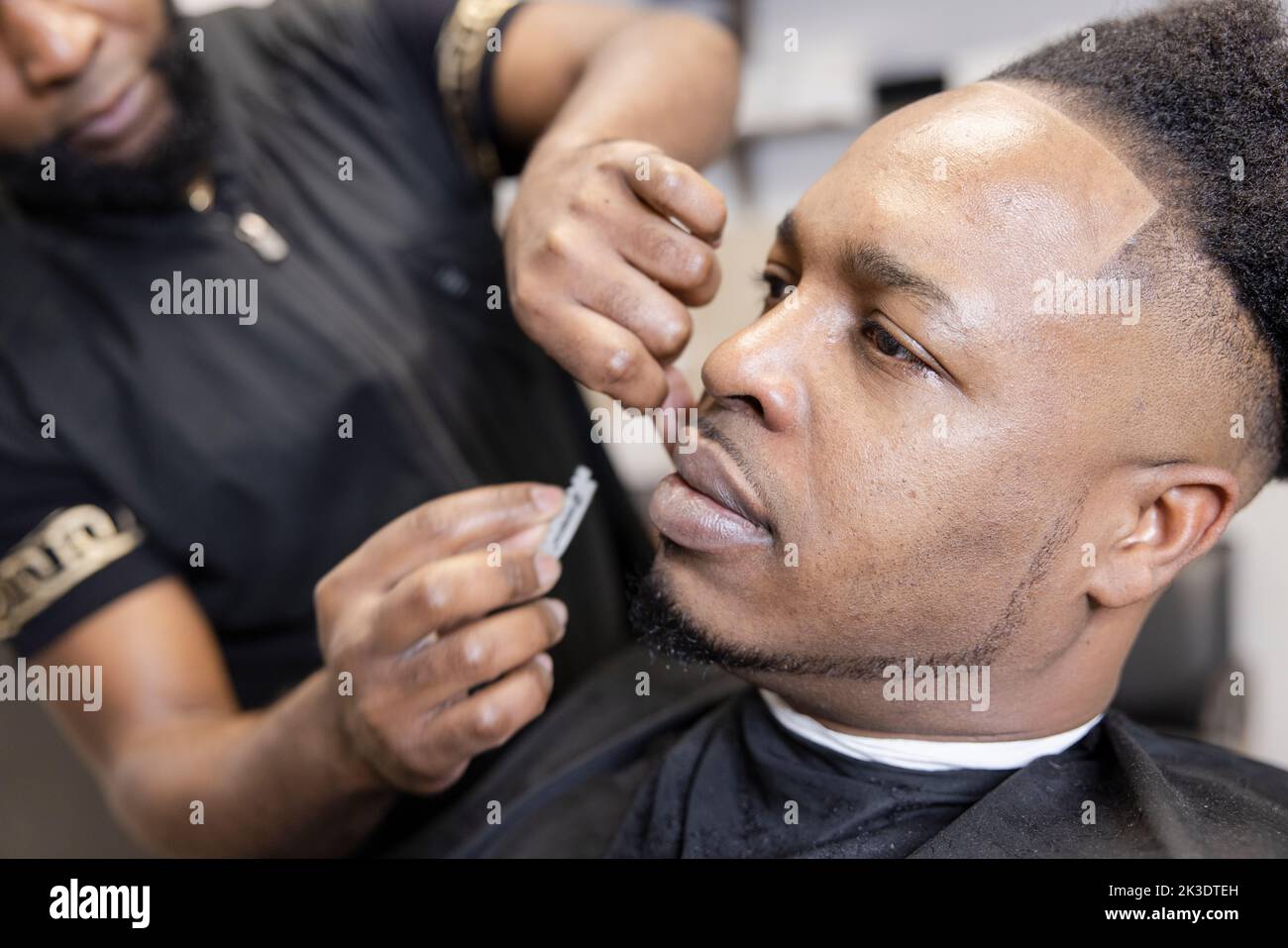 Close up barber with razor blade shaving customer face in barber shop Stock Photo