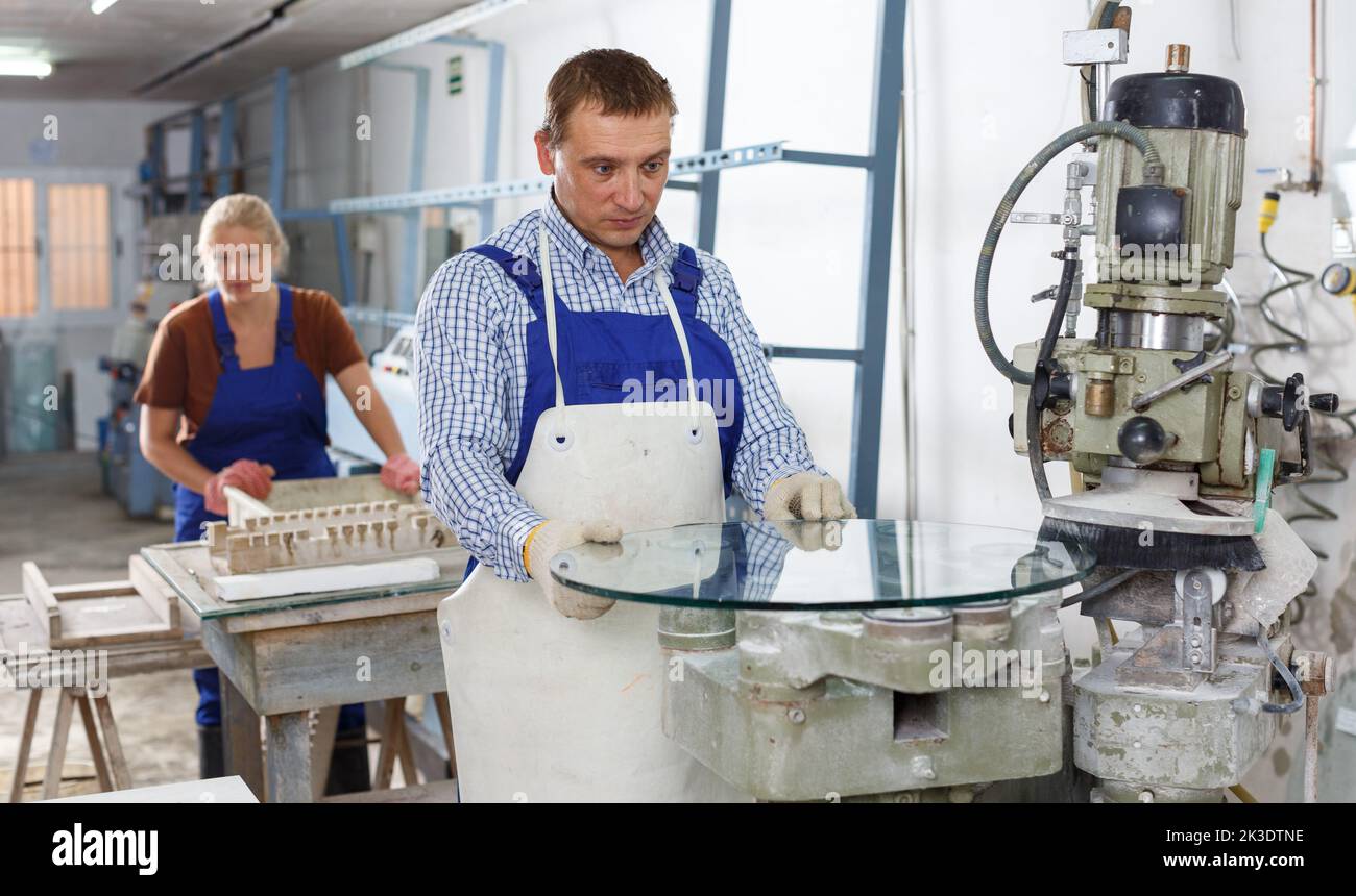 Man working on curved glass beveling machine Stock Photo