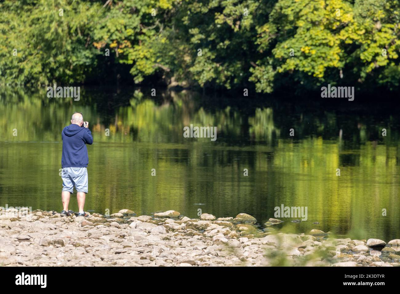 Man taking a photograph of reflections on the River Wharfe, West Yorkshire, England, UK Stock Photo