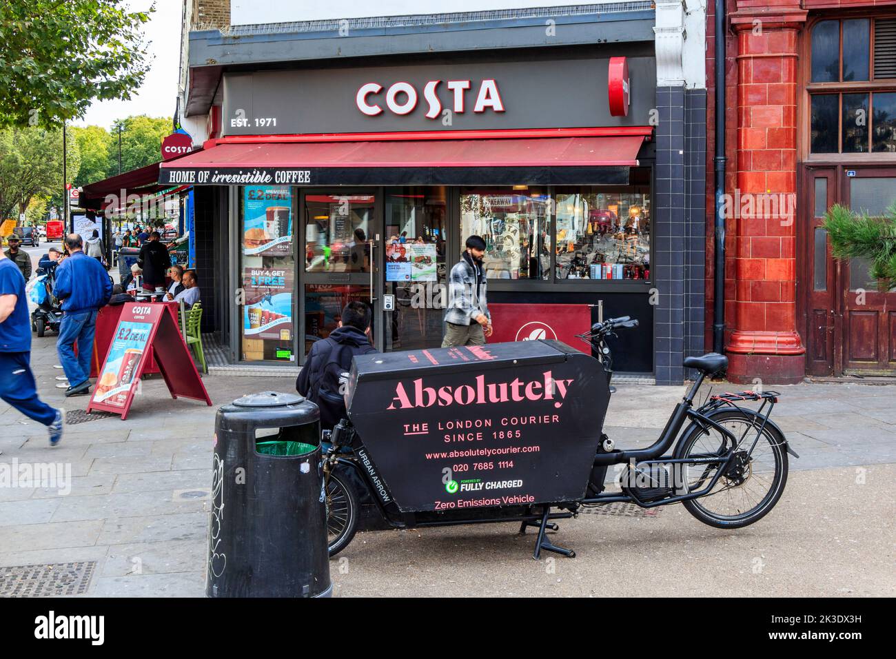 A bicycle courier takes a break outside a Costa coffee shop at Mornington Crescent, Camden, London, UK Stock Photo
