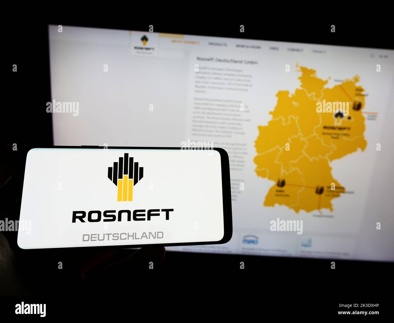 Person holding smartphone with logo of oil refining company Rosneft Deutschland GmbH on screen in front of website. Focus on phone display. Stock Photo