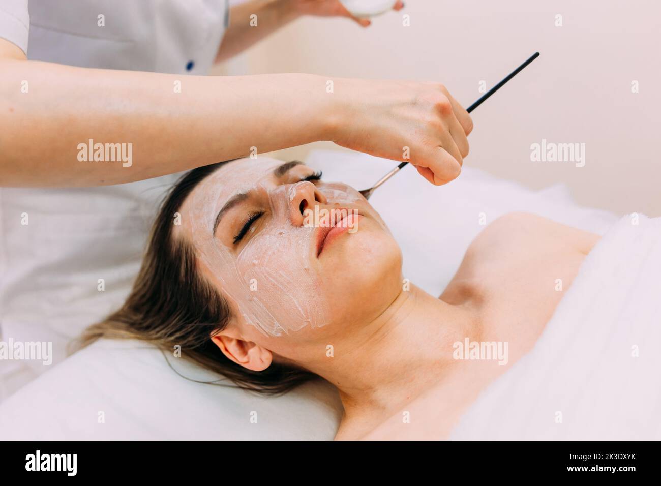 Cosmetologist makes cleansing peeling and face mask for woman. Beauty skin care Stock Photo