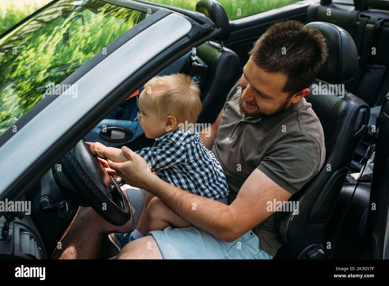 Dad shows his little son how to drive car while sitting behind wheel