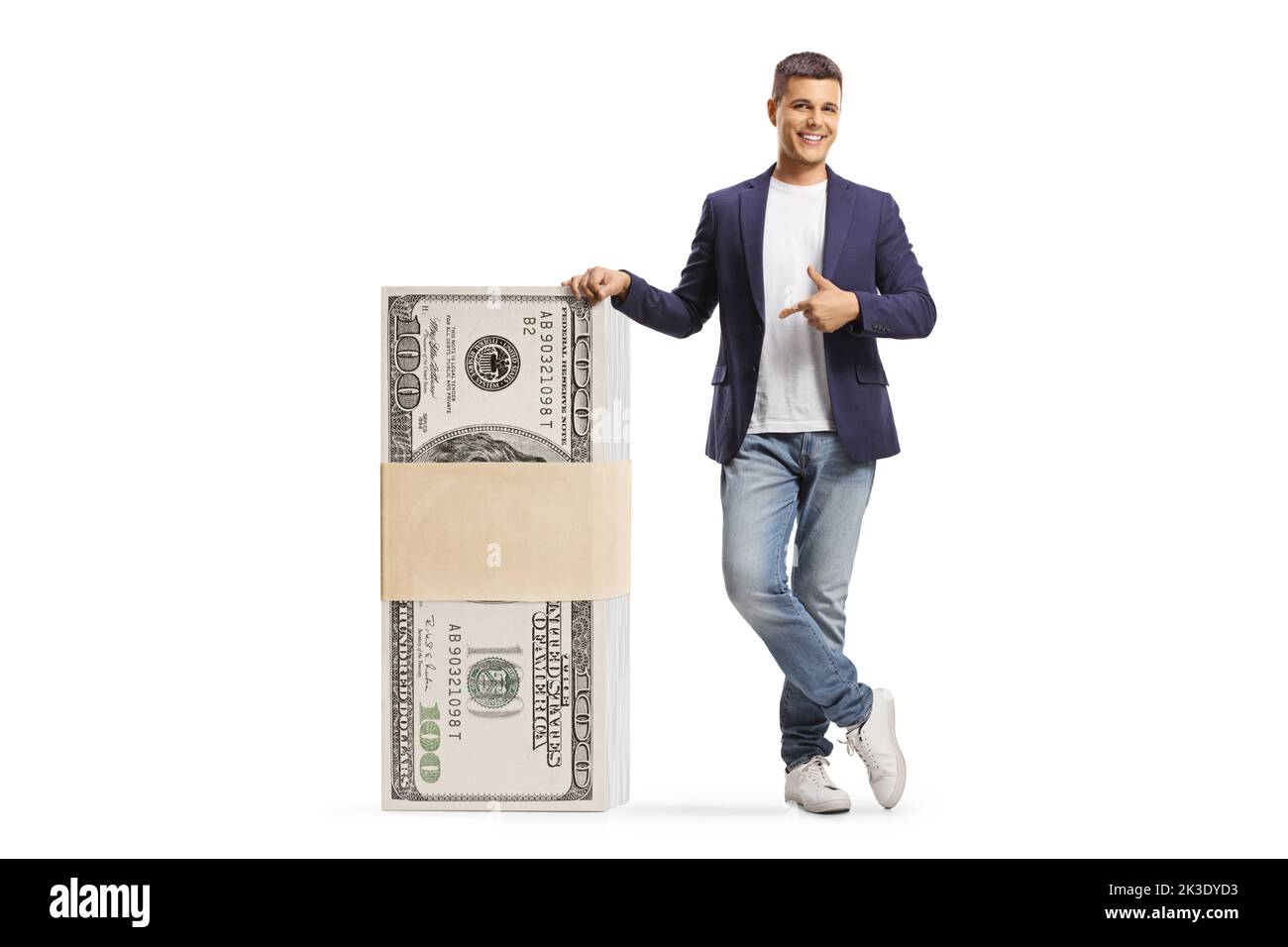 Full length portrait of a young man leaning on a stack of dollar banknotes and pointing isolated on white background Stock Photo