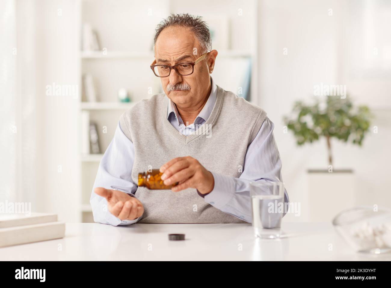 Pensive mature man at home taking pills from a bottle Stock Photo