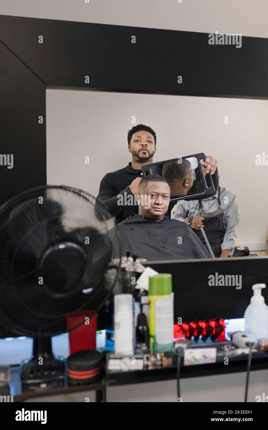 Barber with mirror showing customer haircut in barber shop Stock Photo Alamy
