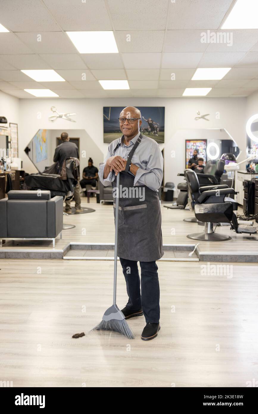 Portrait confident senior barber shop owner sweeping with broom Stock