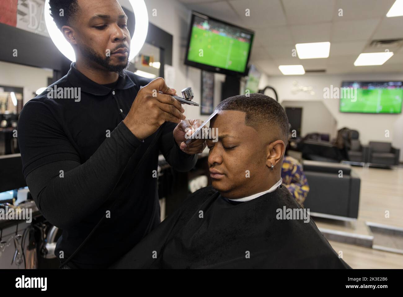 Barber using airbrush on hairline of customer in barber shop Stock Photo