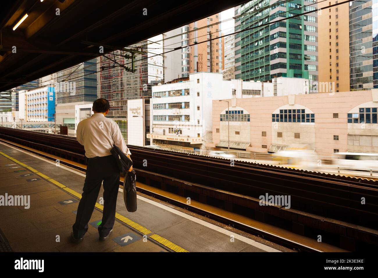Kowloon Bay, Hong Kong, China, Asia - Man waiting for the train at railway station with buildings of Kowloon Bay district. Stock Photo